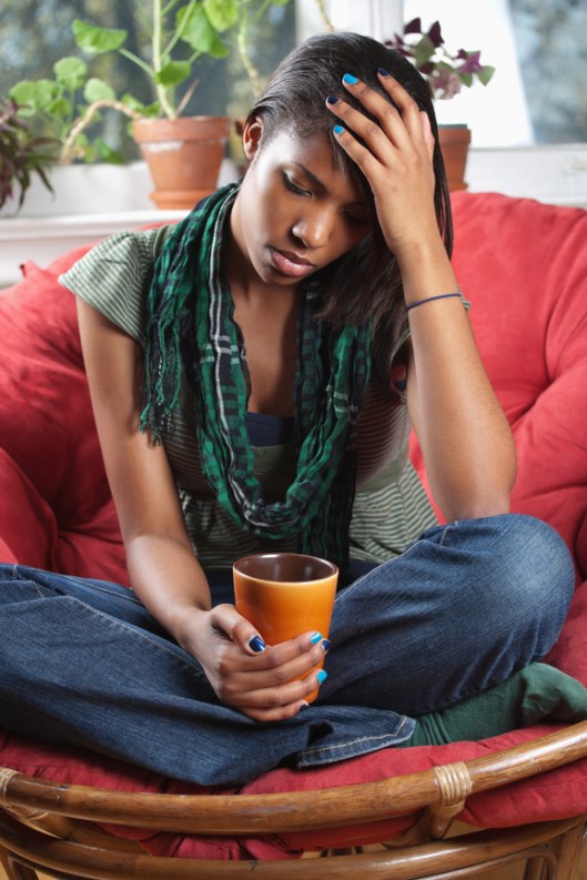 Photo of a sad woman sitting on a chair holding a drink.